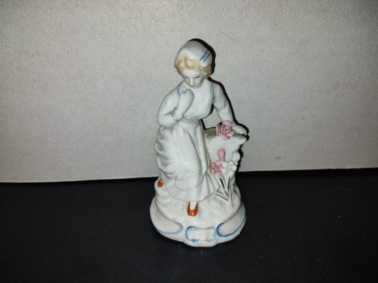 A5- Pieza Vintage De Porcelana. Mujer Sentada De Semblante Serio Junto Pared Ladrillos Y Rosas, 70'S