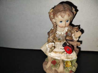 A6- Figura De Resina: Niña De Trenzas Sentada En Banca De Madera Con Mariquita En Las Piernas - 80'S