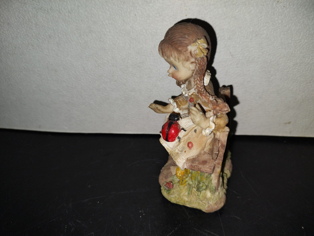 A6- Figura De Resina: Niña De Trenzas Sentada En Banca De Madera Con Mariquita En Las Piernas - 80'S